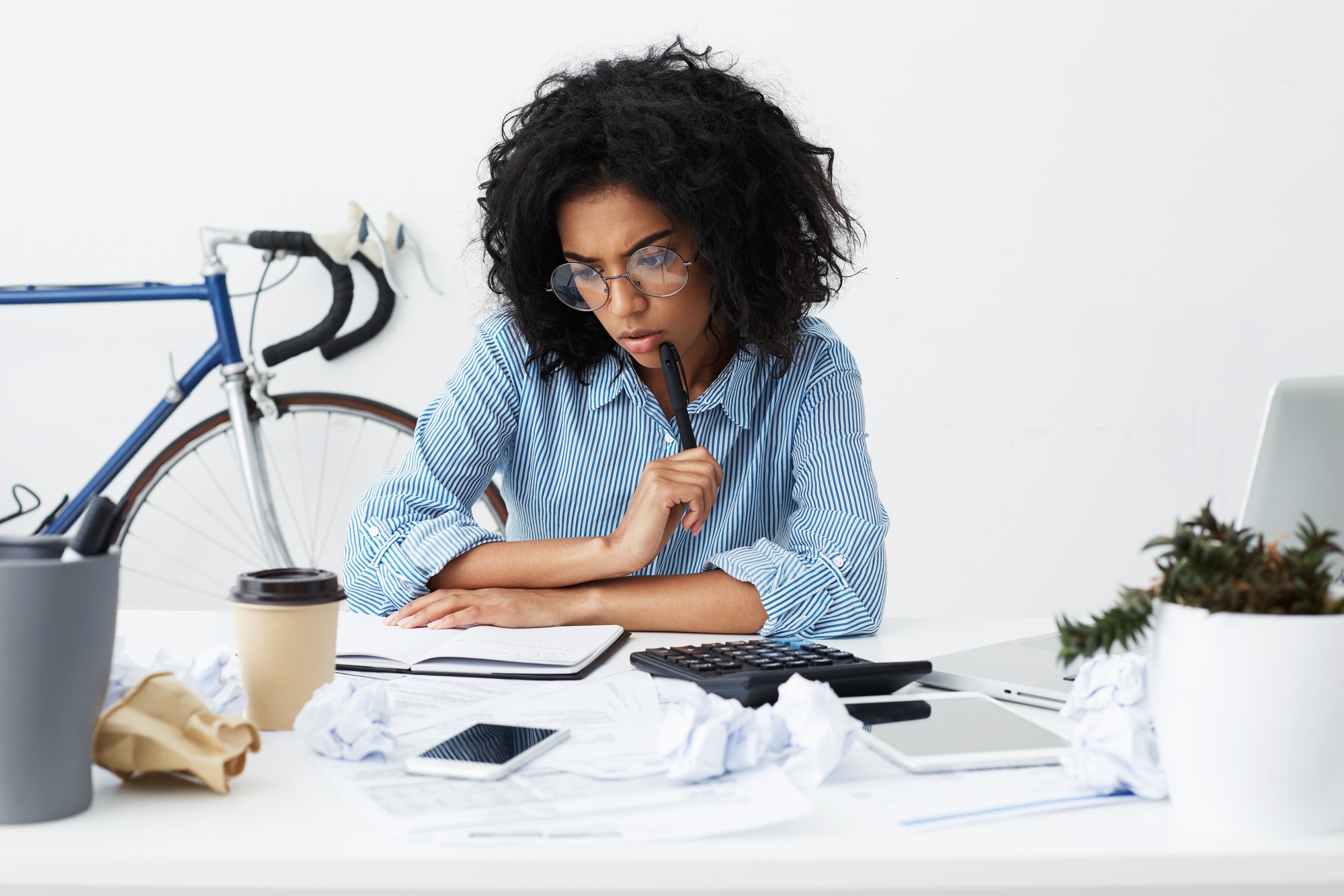 Concentrated female marketing expert holding pen, looking thoughtful while working over new business